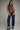 Woman wearing a brown sleeveless top and blue jeans against a gray background