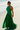 Woman in a green dress standing on a sandy beach.