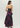 A woman shown from the back wearing a strapless black maxi dress with a bold magenta and purple floral print, photographed against a light gray studio background.