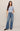 Woman wearing a light blue button-up shirt and blue jeans on a beige background