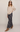 A model wearing a beige V-neck knit sweater and a navy blue plaid maxi skirt, styled with tan ankle boots and sunglasses, against a plain light gray studio background.