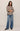 Woman wearing a beige shirt and blue jeans on a plain background