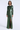 A woman modeling a floor-length, long-sleeve metallic green gown with a draped gathered waist and a high front slit, photographed against a clean light gray studio background.