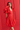 Woman wearing a red dress with puffed sleeves against a red wall.