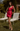 Woman in a red dress standing in a garden with white chairs.