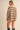 A woman shown from the back wearing an oversized beige knit sweater with horizontal navy stripes, paired with black knee-high boots, against a solid beige studio background.