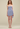 Woman wearing a strapless, pleated blue dress against a beige background