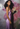 Woman in a purple dress with pink wings standing against a textured wall.