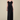 A woman modeling a strapless black evening gown with a ruffled sweetheart bodice and a floor-length pleated skirt, photographed against a plain warm beige studio background.