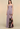 A woman models a strapless floor-length gown in a studio setting. The dress is a muted dusty lavender-purple with a dramatic abstract print in brown, black, and pink on the lower skirt.