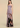 A strapless floor-length gown with a ruched sweetheart bodice and a pleated skirt featuring a large abstract print in brown, black, and muted pink on a lavender base, shown on a model against a warm beige studio background.