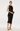 A model wears a black halter-neck midi dress with lace trim at the neckline, hem, and sides, styled with black strappy heels and a black clutch bag against a plain white studio background.