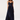 A woman modeling a navy blue maxi dress with a pleated skirt, lace-trimmed spaghetti straps, and a sweetheart neckline, photographed against a plain light gray studio background.