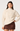A woman modeling a cream cable-knit mock neck sweater with textured geometric patterns on the chest, paired with a brown mini skirt, against a light gray studio background.
