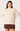 A woman modeling a cream cable-knit mock neck sweater with a brown mini skirt against a light gray studio background.