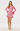 A woman modeling a pink long-sleeve lace mini dress with flared cuffs and a ruffled hem, paired with beige heels, against a plain light gray studio background.