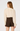 A woman shown from the back wearing a cream-colored blouse with lace detailing on the shoulders and cuffs, paired with dark brown shorts, against a plain white studio background.