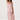A woman modeling a light pink ruffled maxi dress with a dusty rose floral print, photographed against a plain light gray studio background.