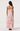 A woman shown from the back wearing a light pink spaghetti-strap maxi dress with a dusty rose floral print and a tiered ruffle skirt, paired with black heels, against a plain white studio background.