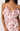 A close-up of a woman wearing a light pink ruffled camisole dress with a dusty rose floral print and thin spaghetti straps.