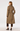 A woman shown from the back wearing a mid-length brown and beige checkered coat, paired with dark brown cropped pants and black heels, against a plain light gray studio background.