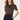 A woman modeling a short-sleeve ribbed knit polo shirt with horizontal brown, beige, and white stripes, paired with dark navy trousers, against a plain white studio background.