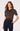 A woman modeling a short-sleeve ribbed knit polo shirt with horizontal brown, beige, and white stripes, paired with dark navy trousers, against a plain white studio background.