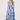 A woman modeling a sleeveless midi dress with a blue and purple floral print on a white background, paired with beige strappy high-heeled sandals, against a light gray studio backdrop.