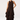 A woman modeling a sleeveless dark brown midi dress with a high neck, front tie detail, and a tiered ruffled skirt, paired with dark brown pointed boots against a light gray studio background.