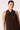 A woman wearing a sleeveless dark brown halter top with a large bow tie at the neck, photographed against a clean light gray studio background.