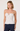 A woman modeling a white spaghetti-strap top with brown polka dots and a ruffled sweetheart neckline, paired with dark blue jeans, against a plain light background.