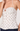A close-up of a model wearing a white spaghetti-strap top with brown polka dots, featuring a ruffled sweetheart neckline and a buttoned front overlay.
