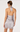 A woman shown from the back wearing a light silver satin halter mini dress with lace trim and a bow at the neck, photographed against a plain light background.