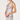 A woman modeling a light silver satin halter mini dress with a draped neckline, lace trim at the hem, and a tie detail at the shoulder, set against a plain light gray studio background.