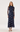 A woman modeling a navy blue long-sleeve midi dress with a sheer mesh overlay and a blue and white floral pattern, paired with black strappy heels against a plain white studio background.