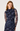 A woman wearing a fitted navy blue long-sleeve dress with a sheer mesh overlay and an allover floral print in purple, blue, and white, photographed against a plain light gray studio background.