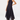 A woman modeling a sleeveless high-neck midi dress with a navy blue base and small white polka dots, paired with brown suede ankle boots against a plain light gray studio background.