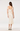A woman viewed from the back wearing a cream satin midi dress with short puff sleeves and a square neckline, paired with black and beige high heels, against a plain white studio background.