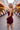 A blonde woman wearing a strapless burgundy romper stands on a cobblestone street lined with restaurants and warm string lights.