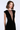 A woman modeling a sleeveless black velvet dress with a deep V-neckline and sheer mesh panel at the chest, photographed against a clean light gray studio background.