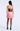 A woman shown from the back wearing a strapless mini dress with a dark sequined bodice and a light pink skirt, paired with black tights and black high heels, against a light gray studio background.