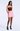 A model wearing a strapless pink mini skirt with a shiny dark brown sequined bodice and black tights, standing against a light gray studio background.