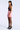 A woman models a strapless mini dress with a dark brown sequined bodice and a light pink skirt, paired with sheer black tights and black high heels, against a light gray studio background.