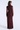 A woman viewed from the back wearing a long-sleeve, high-neck maxi dress in a deep burgundy or maroon shade with a textured, shimmering surface. The dress has a fitted waist and a sheer mesh overlay on the sleeves.