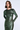 A woman modeling a long-sleeve, metallic dark green bodycon dress with a draped, gathered skirt detail, set against a light gray studio background.
