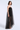 A woman modeling a strapless black tulle maxi dress with a sheer mesh overlay and a structured black bodice, photographed against a light gray studio background.