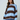 A woman wearing a loose, oversized knit sweater with wide horizontal stripes in light blue, dark brown, and navy blue, paired with light blue pants, against a plain light gray studio background.