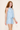 Woman wearing a light blue sleeveless dress with a subtle pattern on a plain background
