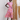 Woman wearing a colorful patterned dress standing against a textured wall.
