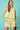 Woman wearing a light yellow sleeveless top and shorts against a teal background